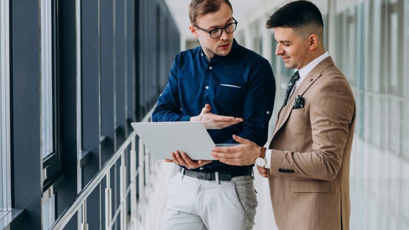 Two male colleagues at the office,standing with laptop